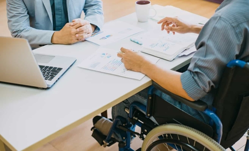 Employee in a wheelchair speaking to someone at a desk.